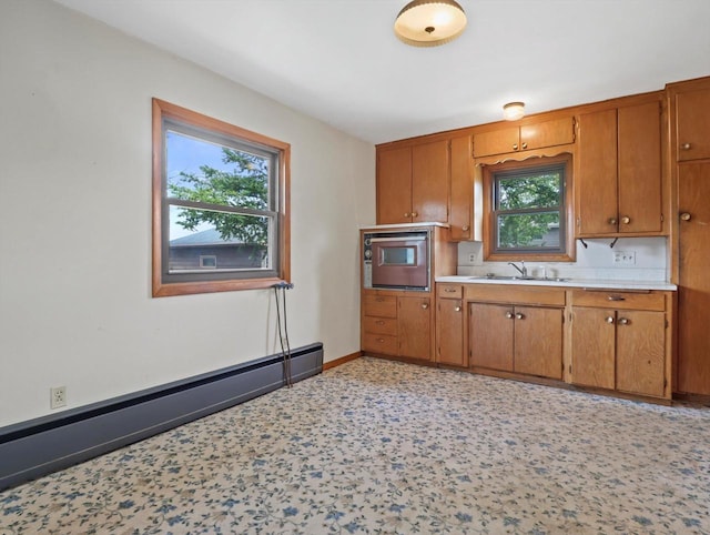 kitchen with brown cabinets, light countertops, a sink, a baseboard radiator, and stainless steel oven