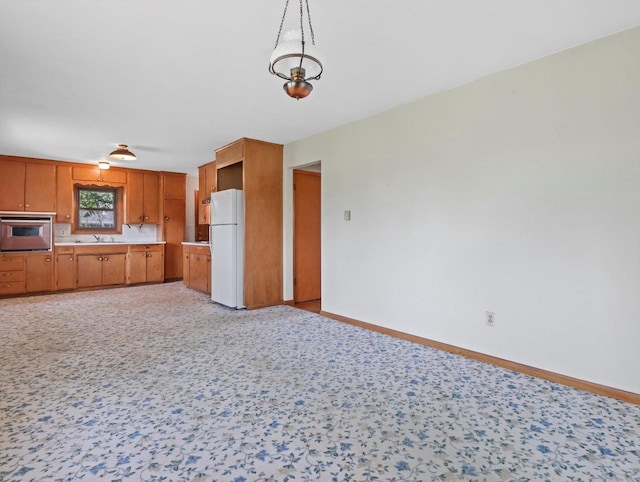 kitchen featuring freestanding refrigerator, oven, baseboards, light countertops, and brown cabinets