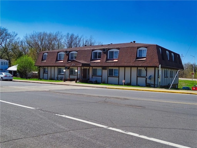 view of front of property featuring roof with shingles, board and batten siding, mansard roof, and uncovered parking