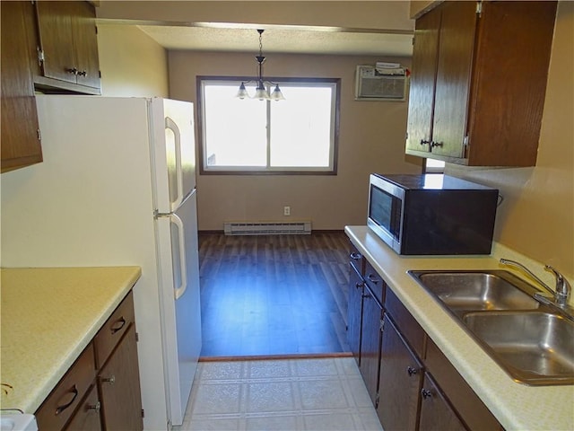 kitchen featuring freestanding refrigerator, a baseboard radiator, light countertops, a wall unit AC, and a sink