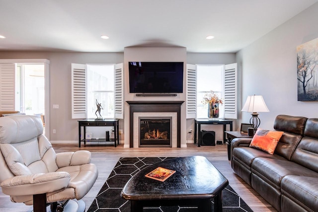 living room featuring a glass covered fireplace, wood finished floors, baseboards, and recessed lighting