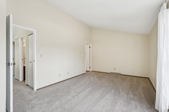 carpeted spare room featuring baseboards and vaulted ceiling