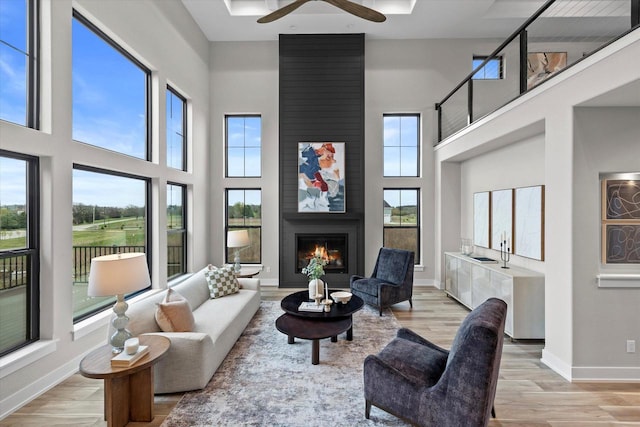 N59W27328 Autumn Ct, Lisbon, WI 53089 - living room featuring ceiling fan, a large fireplace, baseboards, light wood-type flooring, and a towering ceiling