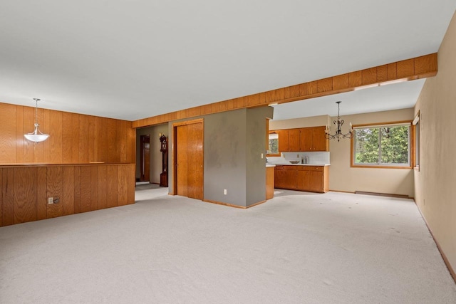 unfurnished living room featuring a chandelier, light carpet, and wood walls