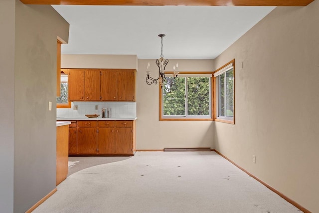 kitchen featuring a notable chandelier, decorative backsplash, brown cabinets, light countertops, and light colored carpet