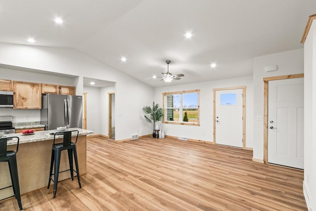 kitchen featuring a kitchen breakfast bar, light wood-style flooring, stainless steel appliances, a ceiling fan, and lofted ceiling