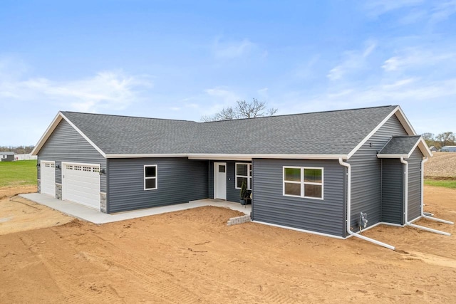 ranch-style home featuring a garage, dirt driveway, and roof with shingles
