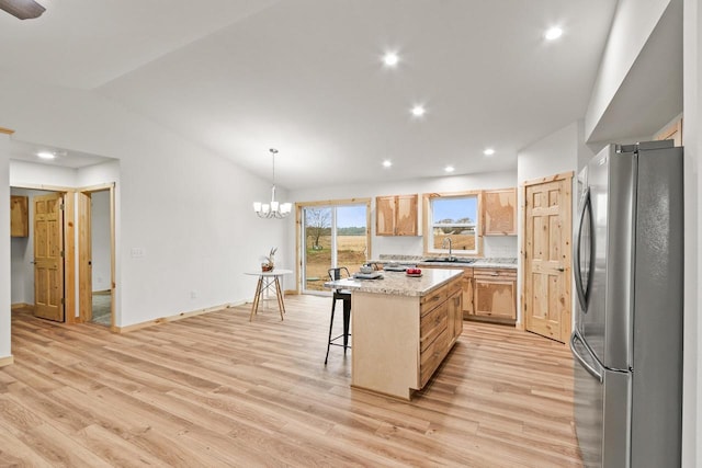 kitchen with a sink, a breakfast bar area, freestanding refrigerator, light wood-type flooring, and vaulted ceiling
