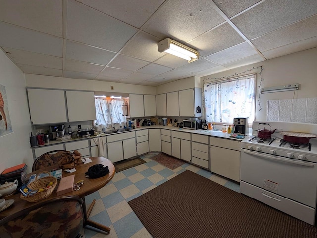 1320 N 2nd St, Wausau, WI 54403 - kitchen with light floors, white range with gas cooktop, a drop ceiling, and white cabinets