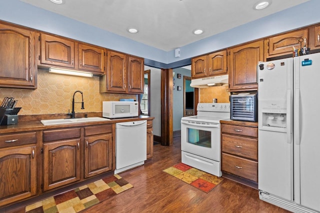 kitchen featuring a sink, white appliances, decorative backsplash, dark wood-type flooring, and under cabinet range hood