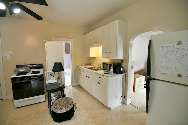 kitchen with gas stove, light countertops, arched walkways, freestanding refrigerator, and stainless steel microwave