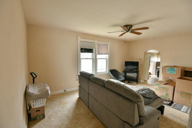 living area with light colored carpet, arched walkways, baseboards, and ceiling fan