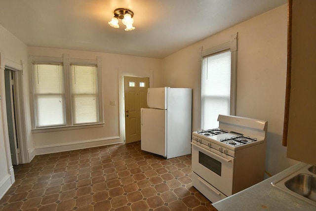 kitchen with white appliances, dark floors, baseboards, and a sink