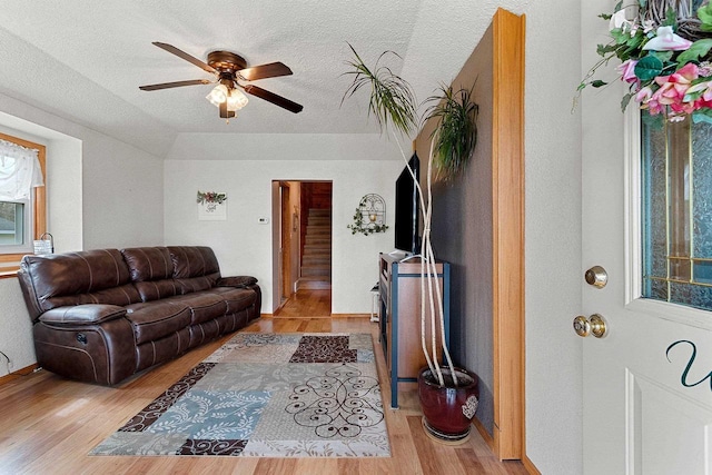 living room with light wood-type flooring, baseboards, ceiling fan, and a textured ceiling