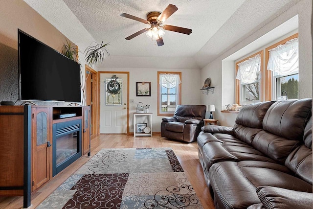 living area featuring light wood finished floors, a textured ceiling, ceiling fan, and a glass covered fireplace