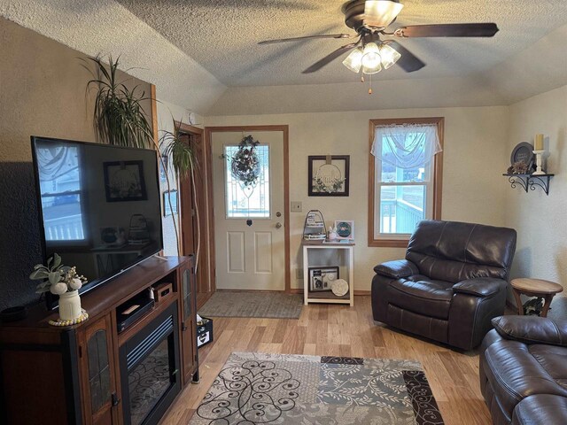 living room featuring lofted ceiling, a textured ceiling, ceiling fan, light wood-style floors, and a textured wall