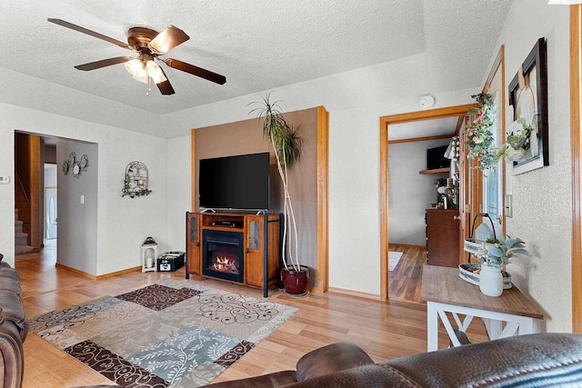living room featuring a textured ceiling, wood finished floors, ceiling fan, and a glass covered fireplace