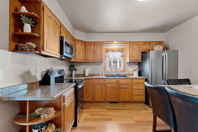 kitchen featuring brown cabinetry, a sink, open shelves, stainless steel appliances, and light wood-type flooring