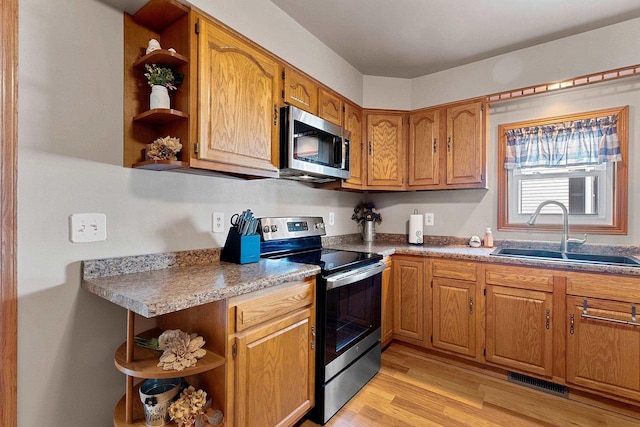 kitchen featuring open shelves, appliances with stainless steel finishes, light wood-style flooring, and a sink