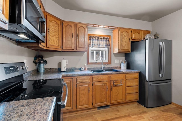 kitchen with brown cabinets, stainless steel appliances, light wood-type flooring, and a sink