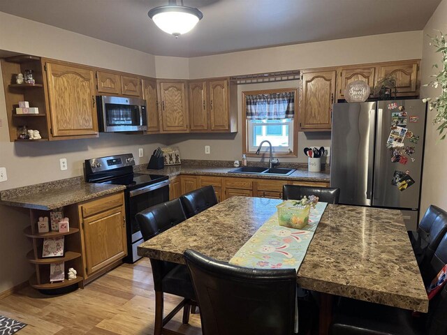 kitchen featuring brown cabinetry, light wood finished floors, a sink, open shelves, and appliances with stainless steel finishes