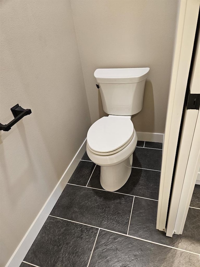 bathroom featuring baseboards, tile patterned flooring, and toilet