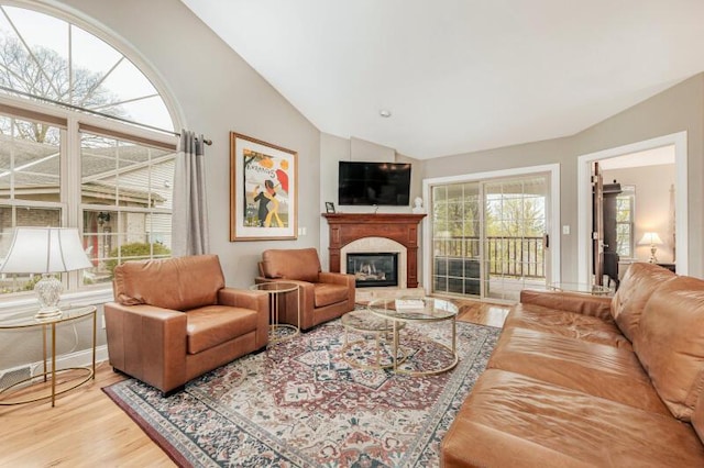 living room with baseboards, a glass covered fireplace, wood finished floors, and vaulted ceiling