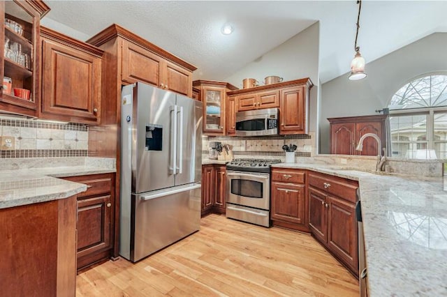 kitchen featuring lofted ceiling, brown cabinets, a sink, light wood-style flooring, and appliances with stainless steel finishes