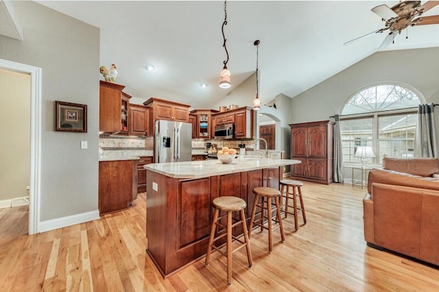 kitchen featuring ceiling fan, brown cabinetry, a kitchen bar, appliances with stainless steel finishes, and arched walkways