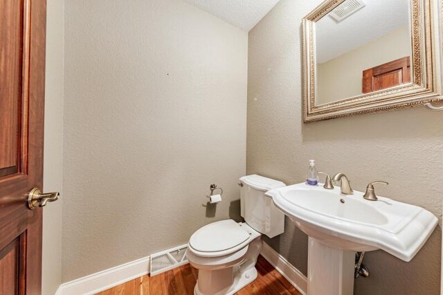 half bath featuring visible vents, baseboards, wood finished floors, and toilet