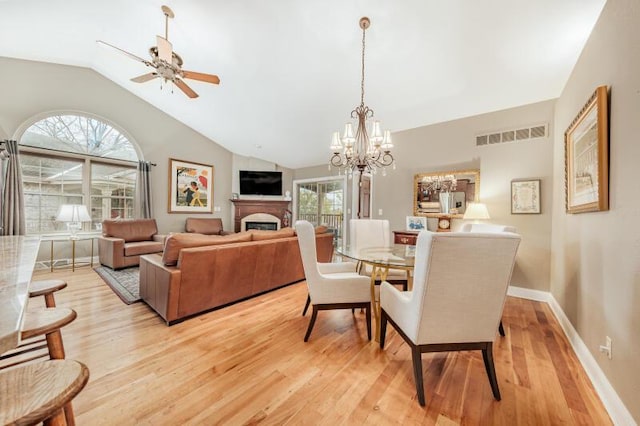 dining room with light wood finished floors, a fireplace, ceiling fan with notable chandelier, vaulted ceiling, and visible vents