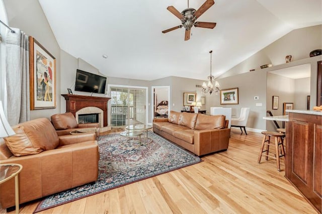 living room featuring a glass covered fireplace, light wood-style flooring, ceiling fan with notable chandelier, baseboards, and lofted ceiling