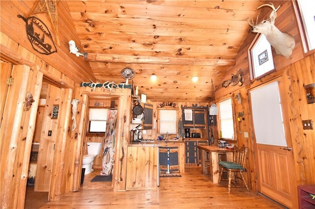 kitchen with vaulted ceiling, a sink, wooden ceiling, wooden walls, and light wood-style flooring