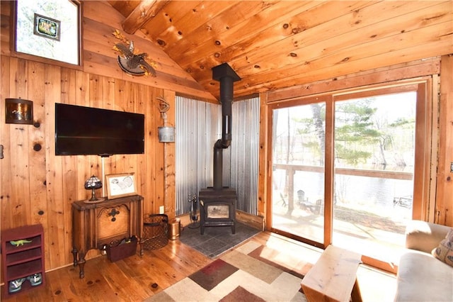living room featuring wooden walls, lofted ceiling with beams, a wood stove, and hardwood / wood-style flooring