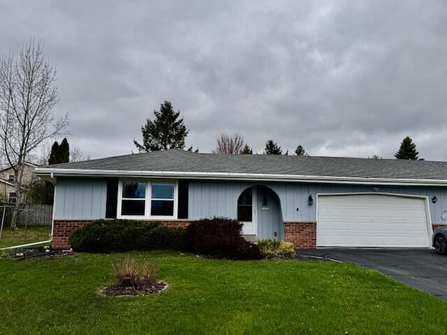 ranch-style home featuring an attached garage, aphalt driveway, a front lawn, and brick siding