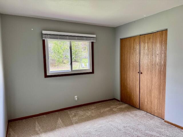 unfurnished bedroom featuring light colored carpet, baseboards, and a closet