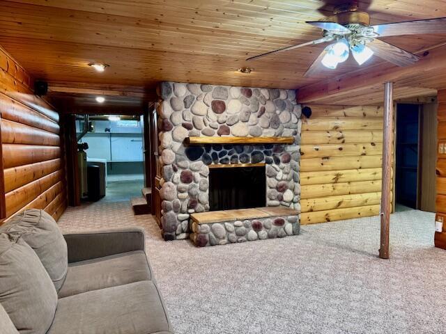 living room with carpet floors, rustic walls, a stone fireplace, wooden ceiling, and a ceiling fan