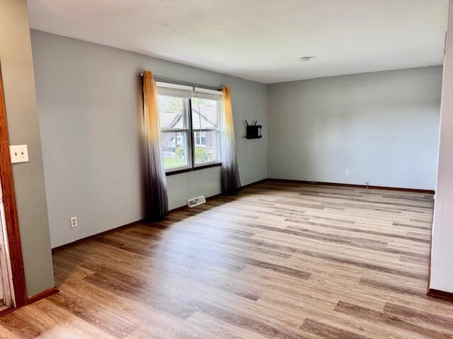 empty room featuring baseboards, light wood-style flooring, and visible vents