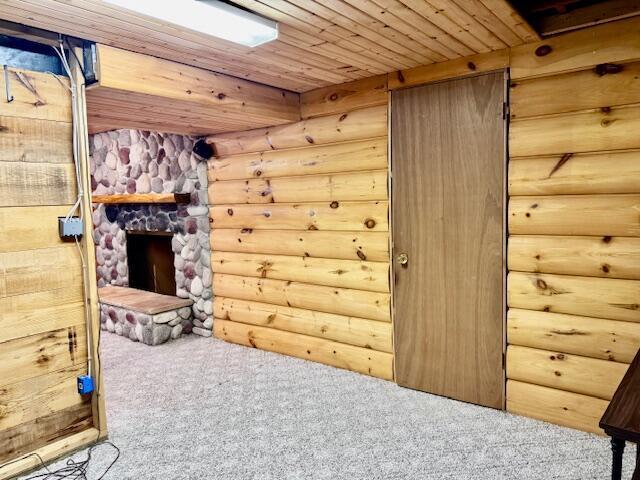 unfurnished room with log walls, a fireplace, carpet flooring, and wood ceiling