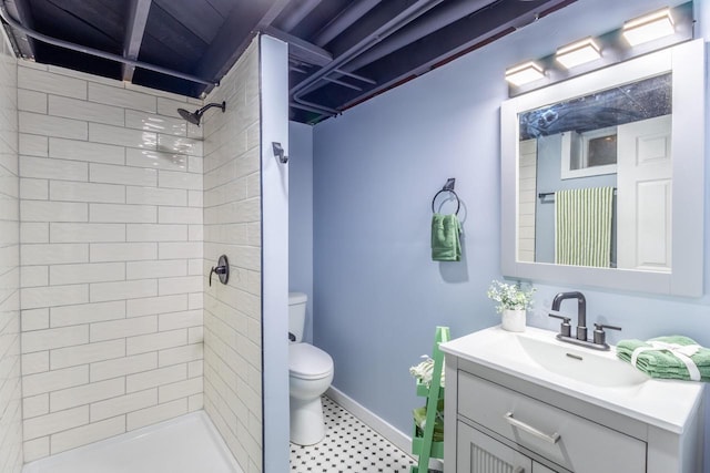 full bathroom featuring toilet, baseboards, tiled shower, and vanity
