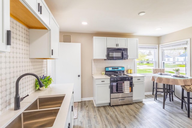 kitchen with black microwave, a sink, stainless steel gas range oven, backsplash, and visible vents