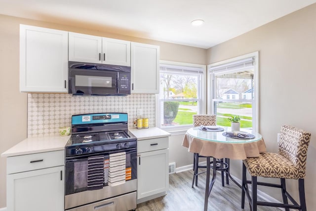 kitchen featuring stainless steel range with gas cooktop, light countertops, light wood-style floors, and black microwave