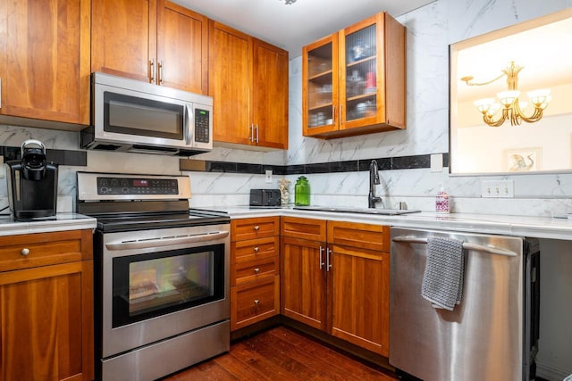 kitchen with appliances with stainless steel finishes, an inviting chandelier, a sink, light countertops, and dark wood-type flooring