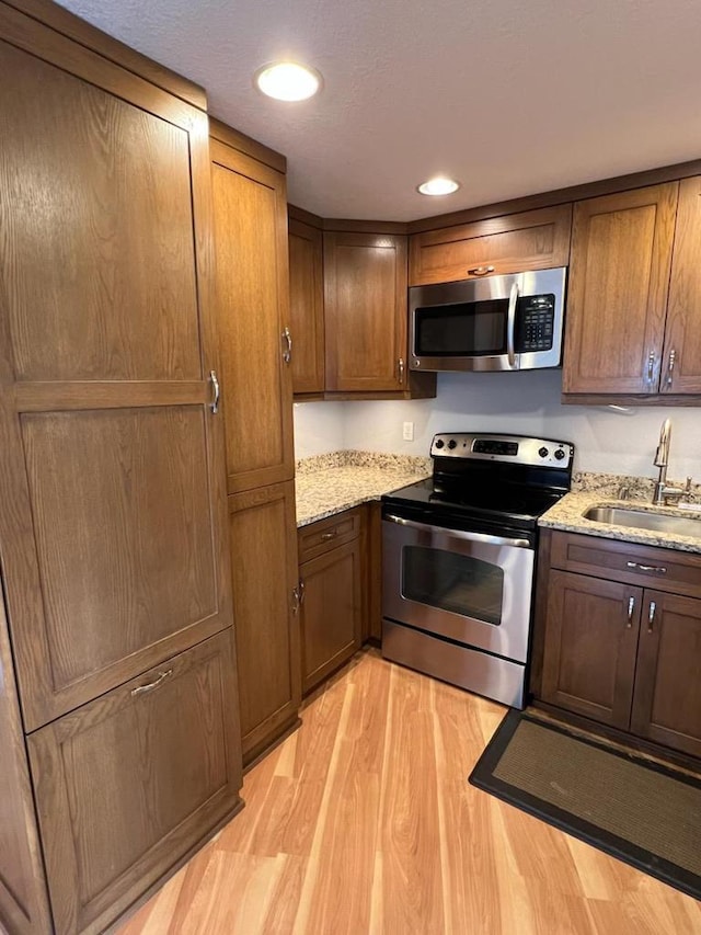 kitchen featuring light stone countertops, light wood-style floors, recessed lighting, a sink, and stainless steel appliances