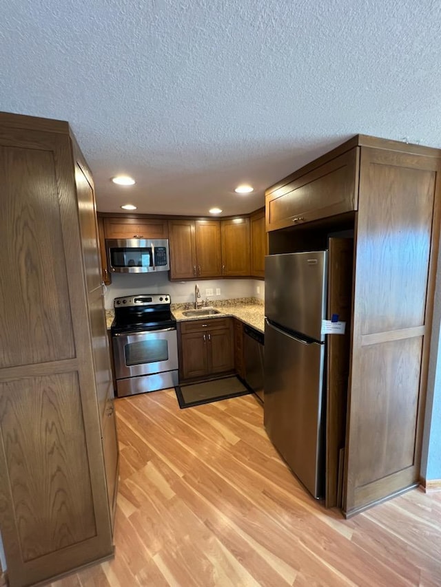 kitchen featuring appliances with stainless steel finishes, a sink, light wood-style floors, a textured ceiling, and recessed lighting