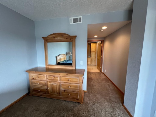 hall featuring a textured ceiling, visible vents, baseboards, and dark colored carpet