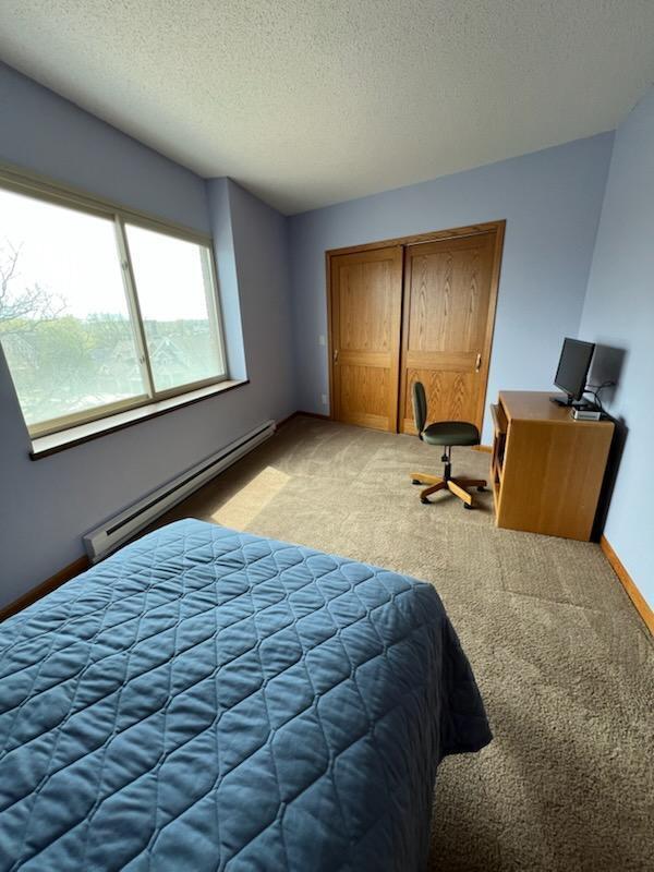 bedroom featuring baseboard heating, a closet, a textured ceiling, and light colored carpet