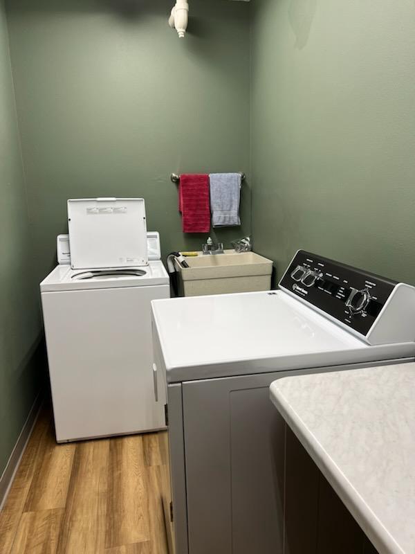 laundry room featuring laundry area, light wood-type flooring, a sink, baseboards, and washer and clothes dryer
