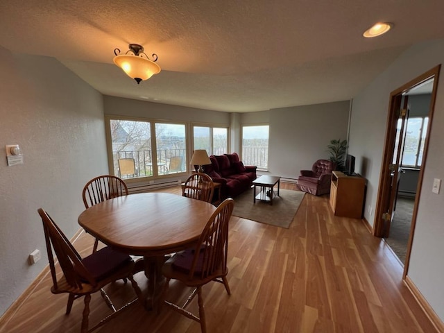 dining space with baseboards, a textured ceiling, and light wood finished floors