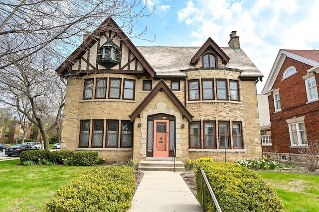 tudor-style house with brick siding, a chimney, and a front yard